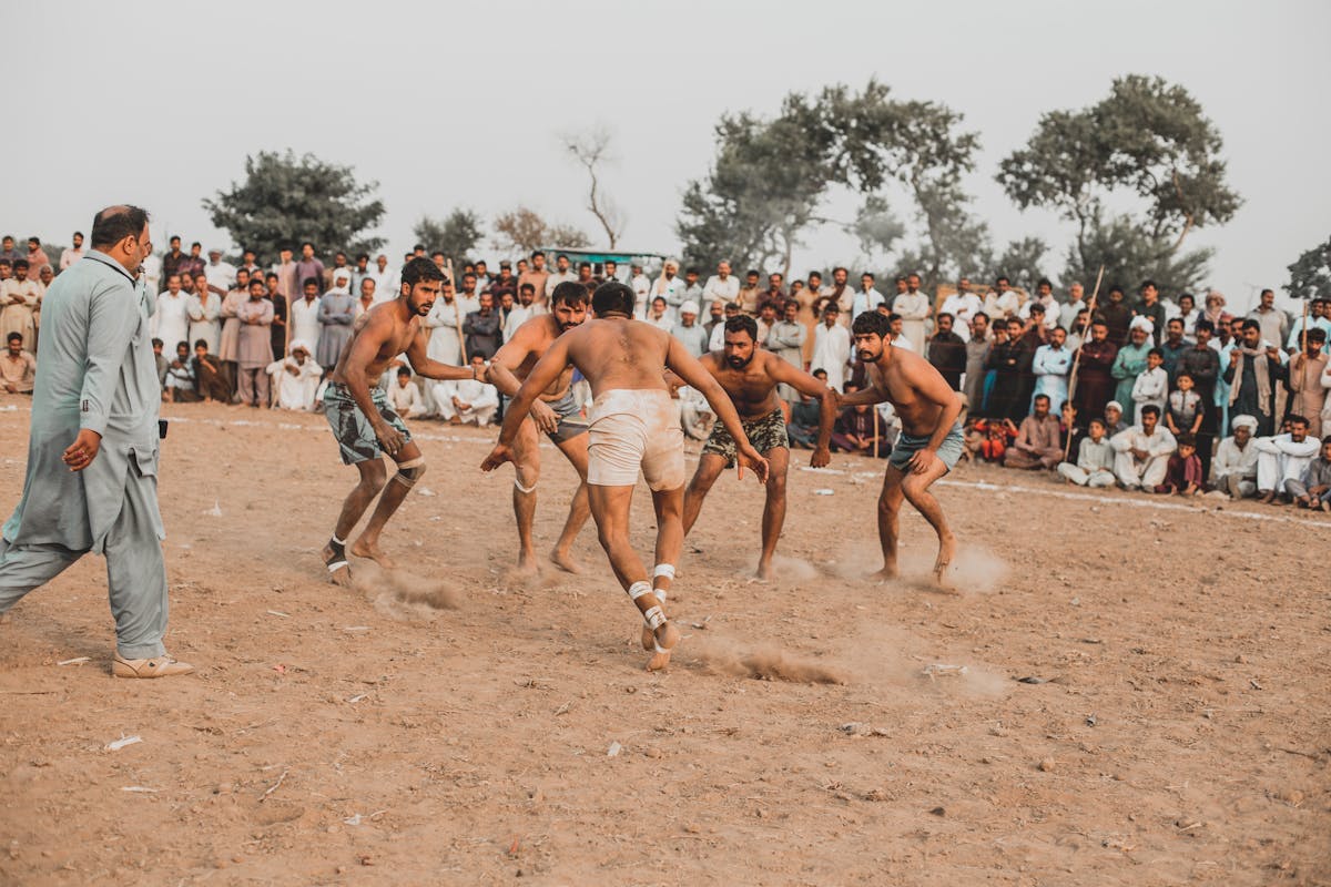 Pakistani kabaddi players in mid-raid on a Punjab dirt ground with village crowd watching